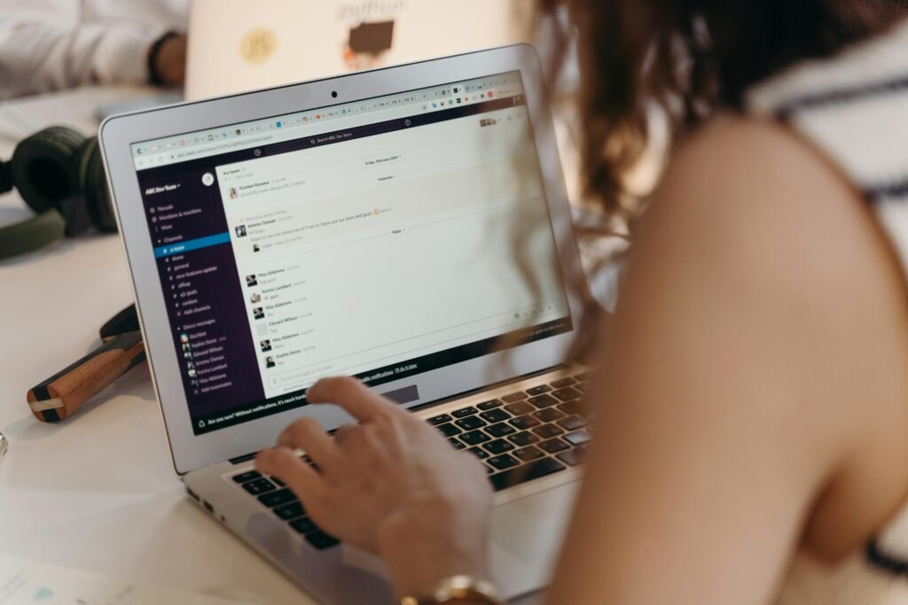 pexels-photo-7439124-7439124 A businesswoman typing on a laptop in an office setting, using Slack for communication.